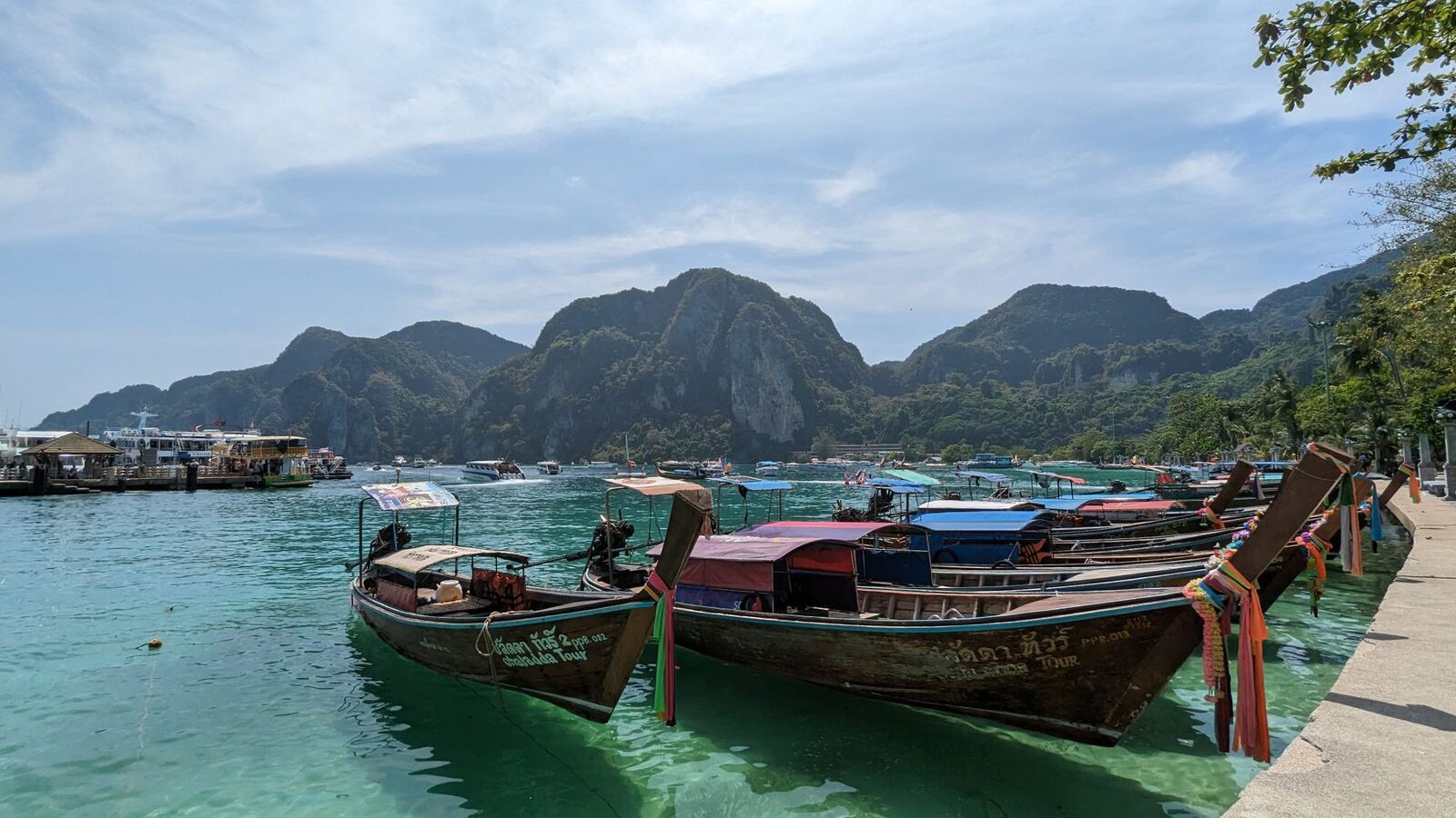 Színes thai longtail hajók a türkizkék vízben, mészkőhegyek előtt.